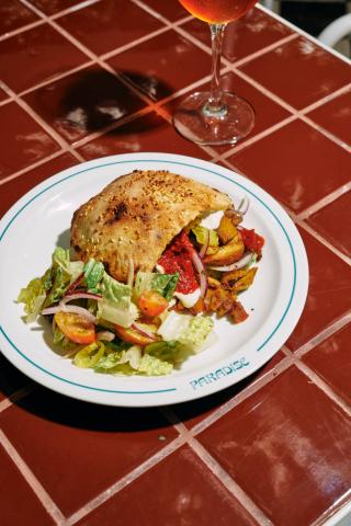The image shows a meal served on a ceramic plate with the word "PARADISE" on the rim, placed on a table with red-brown tiles