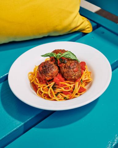 This image shows a plate of spaghetti and meatballs, topped with a fresh basil leaf