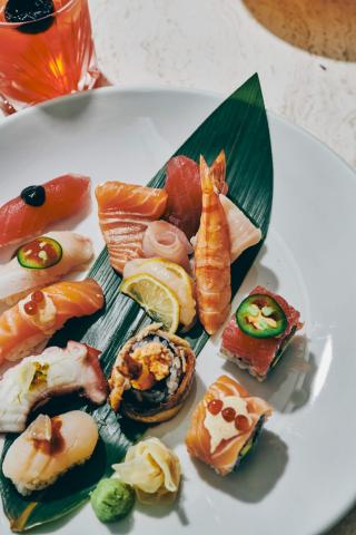 This image displays a variety of sushi and sashimi items arranged attractively on a plate with a green leaf, possibly a banana leaf, underneath