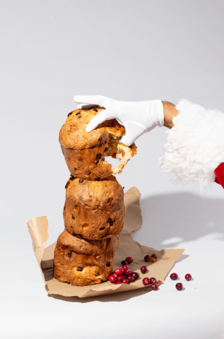 The image features a stack of three traditional panettone breads with what appears to be someone in a Santa Claus costume touching the top loaf