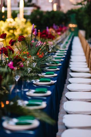 The image shows an elegantly set outdoor dining table, which is long and adorned with colorful flowers and plants as decorations