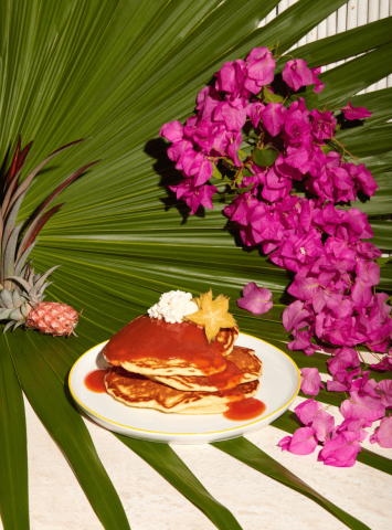 This image features a plate of pancakes topped with a red sauce and a dollop of cream, garnished with a star-shaped piece of fruit