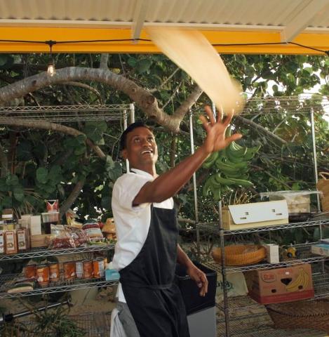 This image features a man, who seems to be a chef or a baker, joyfully tossing a flat, elongated piece of dough in the air
