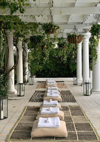 The image shows an elegant outdoor or semi-outdoor spa-like setting with a series of comfortable-looking beds arranged in a row on a tiled floor