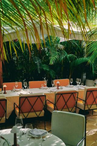 This image features an elegant outdoor dining setting under the shade of vibrant green palm fronds