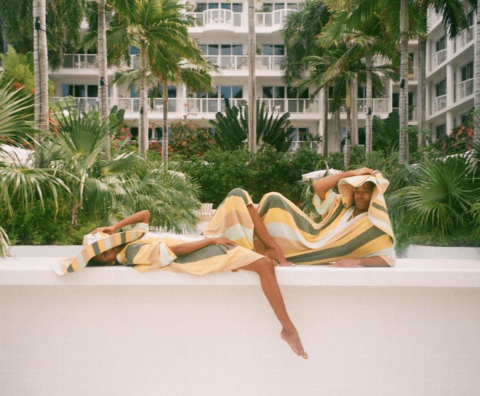 The image shows a person reclining and partially draped with a sunlight patterned fabric, matching their clothing, in what appears to be a relaxing outdoor setting