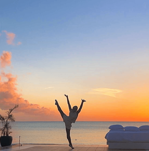 This image features a person performing a cartwheel at sunset on a waterfront deck, likely near a beach