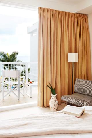 The image features an inviting indoor room with a coastal view visible from a balcony