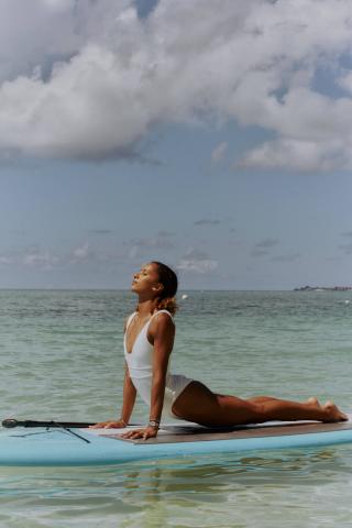 This image depicts a woman performing a yoga pose on a paddleboard in a tranquil sea