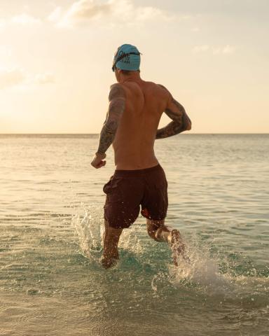 The image shows a man running into the sea at what appears to be sunset