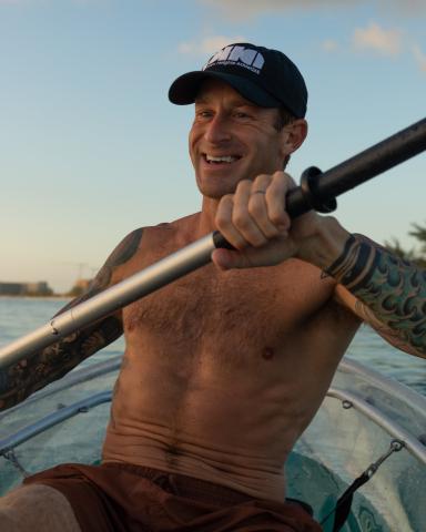 This image features a man rowing a transparent canoe or kayak
