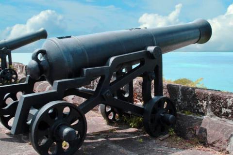 Old-fashioned cannon on stone platform overlooking ocean under clear sky