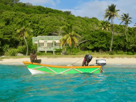 Two people in colorful boat on tropical beach with lush greenery and old structure.