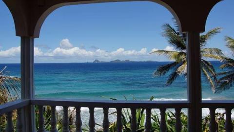 View of turquoise sea through balcony arch with palm trees and distant islands