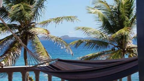 View from balcony with hammock, palm trees, and distant island on a clear day