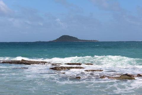Vibrant coastal scene with lush island, rocky shores, and turquoise sea under a partly cloudy sky