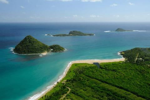 Aerial view of a coastal beach with nearby forest, river, and scattered islands.