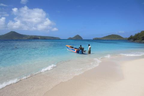 Tropical beach with boat, swimmers, and mountains in the distance