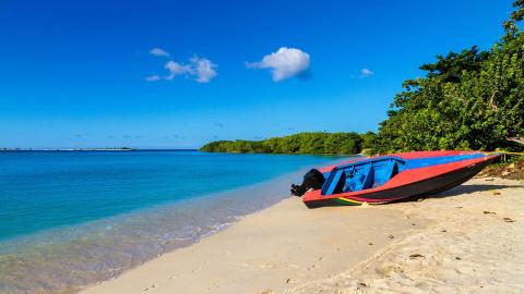 Tropical beach with a colorful boat on white sand, clear blue water, and greenery