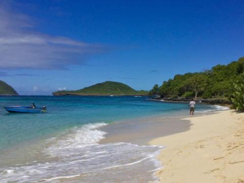 Serene beach with clear waters, white sands, lush greenery, and a small boat