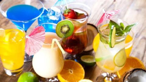 Colorful fruity cocktails with kiwi, lime, and strawberry garnishes on a wooden table.
