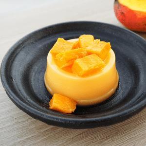 Creamy flan topped with mango chunks on a dark plate, elegant dessert presentation