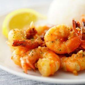 Juicy pan-seared shrimp with herbs, lemon slice, and rice on a plate.