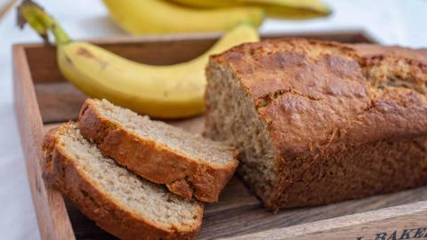 Freshly baked banana bread with slices and whole banana on wooden tray.