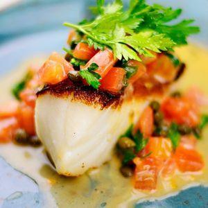 Pan-seared fish with tomato herb topping and creamy caper sauce, garnished with cilantro.