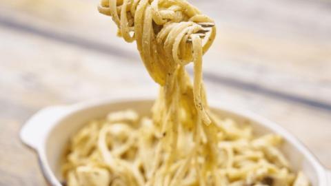 Creamy herb pasta on fork above white bowl on wooden table