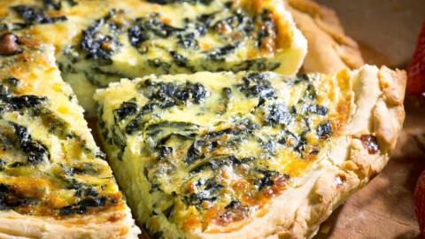 Quiche with spinach, golden crust, and creamy filling, sliced for serving.
