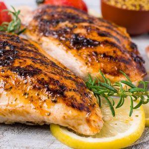 Grilled chicken breasts with lemon and rosemary, sauce and strawberries in background
