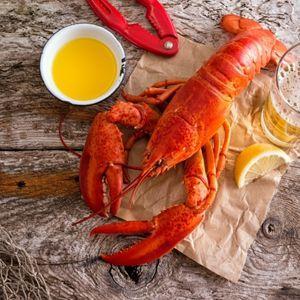 Cooked lobster with melted butter, lemon slices, beer, and crackers on wood.