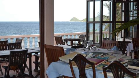 Seaside dining area with ocean view, wooden tables set for guests.