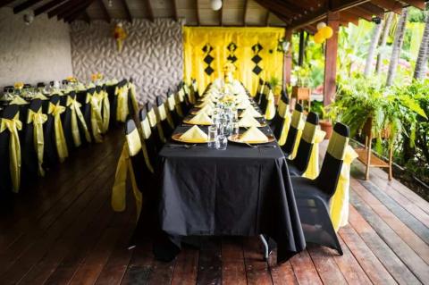 Elegant dining setup with black tablecloths and yellow accents in a rustic venue.