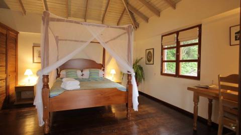 Cozy bedroom with a four-poster bed, wooden decor, and nature view.
