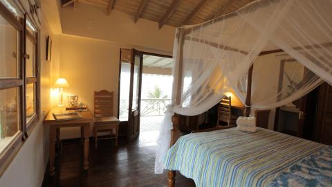 Cozy tropical bedroom with mosquito net, wooden desk, teapot, and lush view
