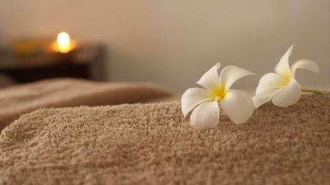 White frangipani flowers on tan towel with candle glow in spa setting