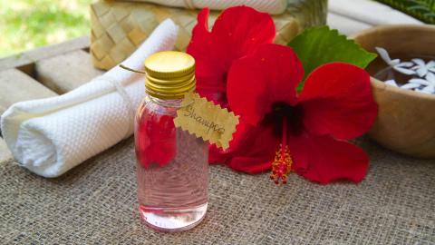 Pink shampoo in glass bottle with hibiscus flower and white towel