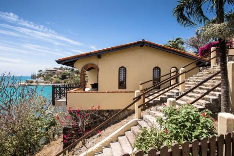 Coastal house with yellow stucco, Spanish tile roof, and sea view