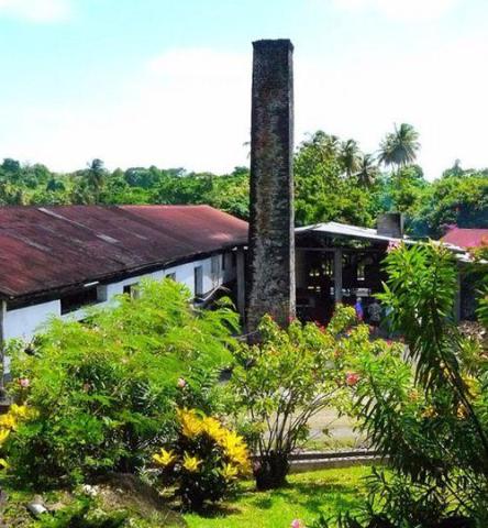 Historic tropical site with old chimney, red-roof buildings, and lush gardens