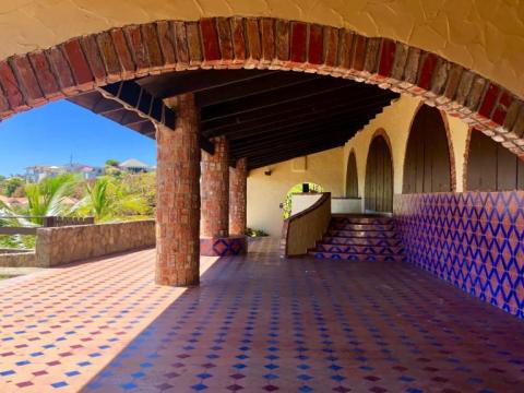 Arched corridor with brick columns, tile roof, and geometric floor in a sunny, lush setting.