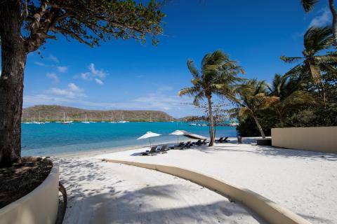 Scenic beach with lounge chairs, white umbrellas, and sailboats under a clear blue sky