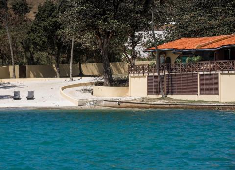 Secluded beachfront property with sandy area, lounge chairs, and calm blue water.