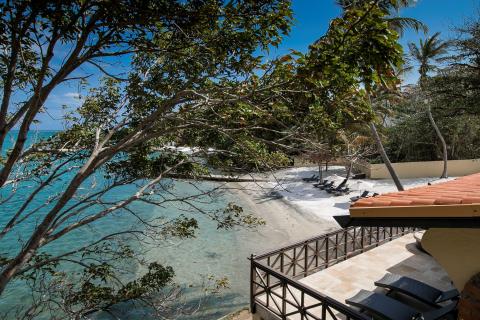 Secluded beach with terracotta roofed building, palm trees, white sand, and clear blue sea