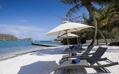 Luxurious beach lounge with white umbrellas and chairs overlooking ocean and boats