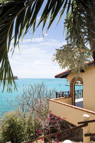 Tropical coastal view with terracotta-roofed building, pier, and moored boat