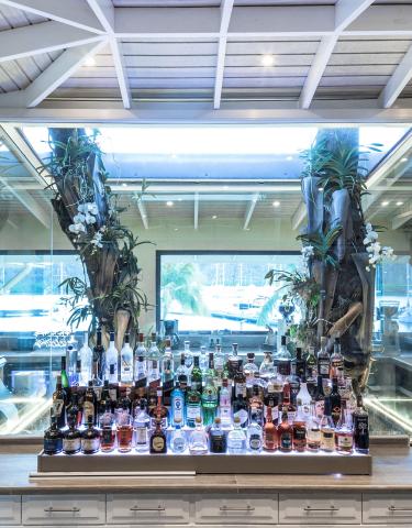 Luxurious bar with tree decor and spirits, white orchids, and scenic view through window.