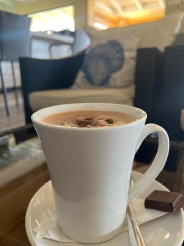 Close-up of hot chocolate in a white cup with cocoa topping on a saucer with chocolate bar.