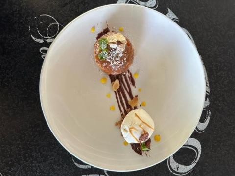 Elegant caramel-glazed cake with gold leaf, mint, ice cream, and chocolate sauce on white plate.